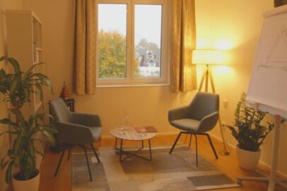 ein Foto der Therapieräumlichkeit, ein Raum mit zwei Sesseln, Pflanzen und Flipchart